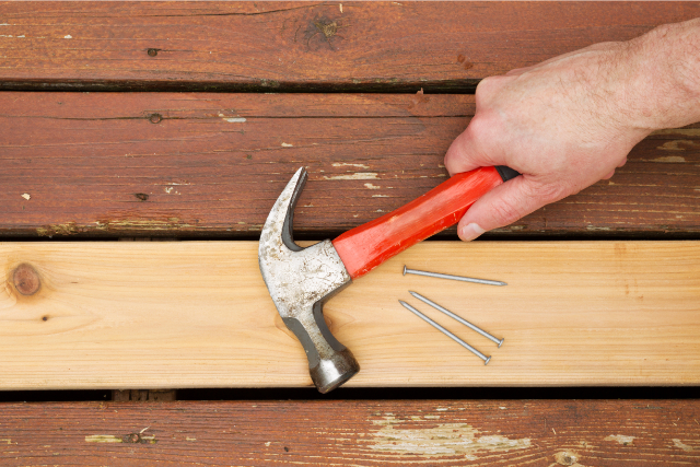 Worker Repairing Old Wooden Boards on Deck with hammer and nails